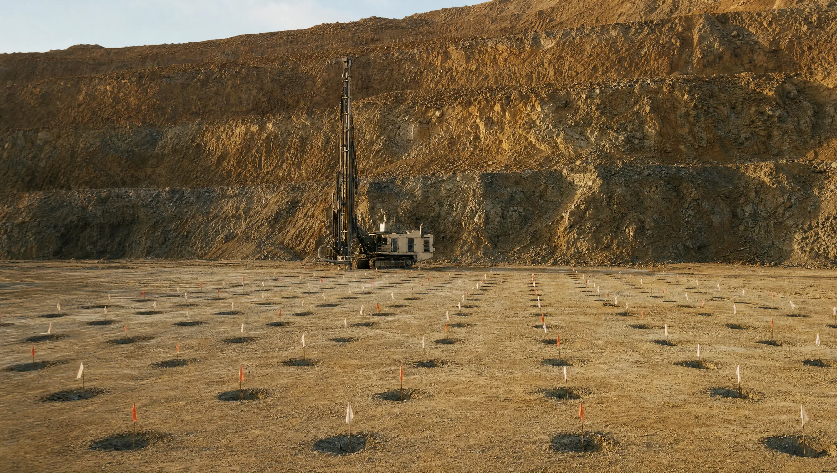 A drill rig on the bench with a laid-out blast pattern, collar positions marked in a clean grid