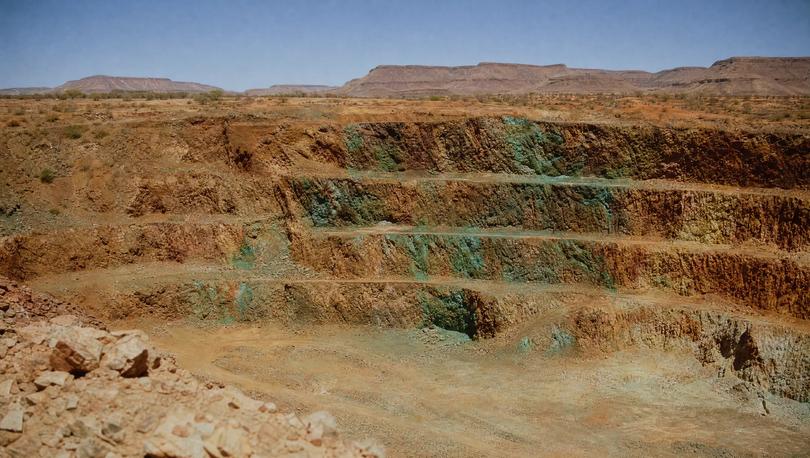 The Kamanjab open pit, wide and cinematic: red-brown oxidised copper benches under hard Namibian light