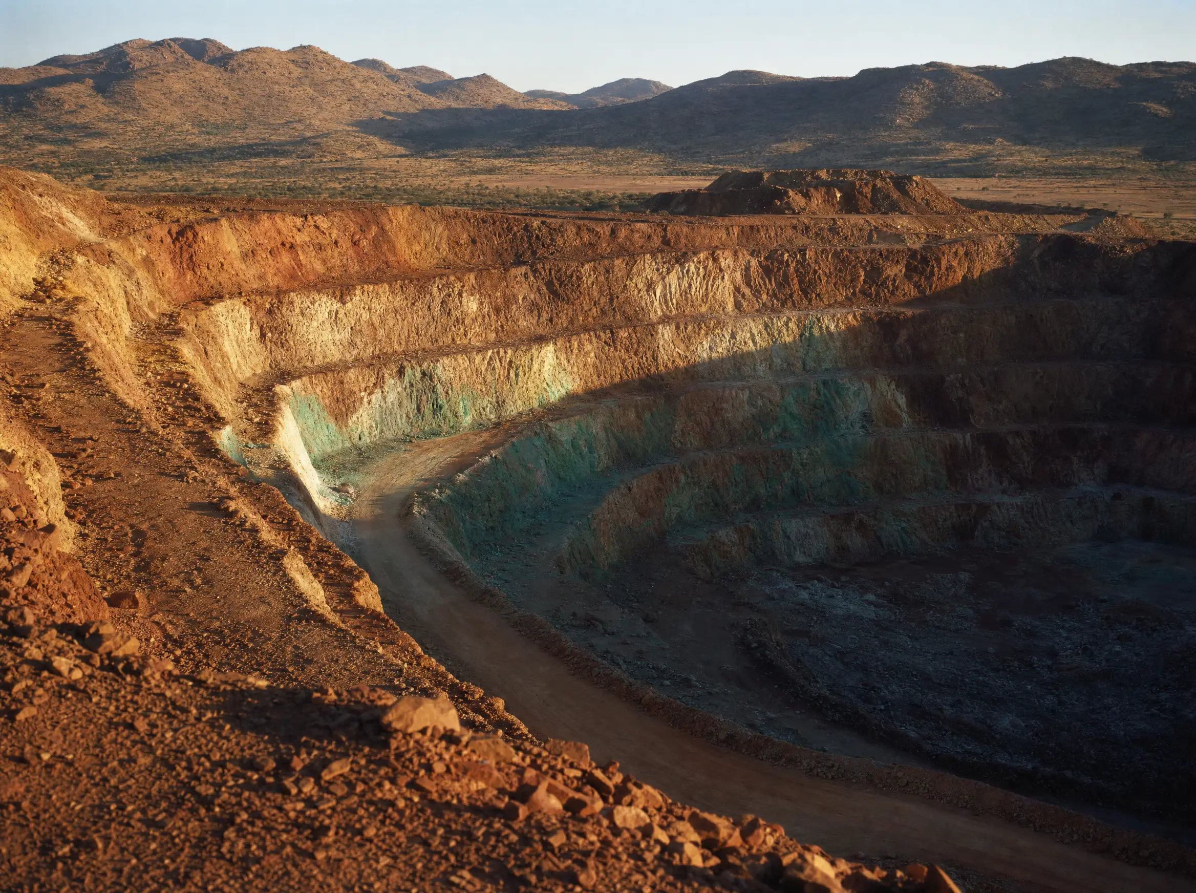 Benched walls of the Kamanjab open pit stepping down through oxidised copper ground
