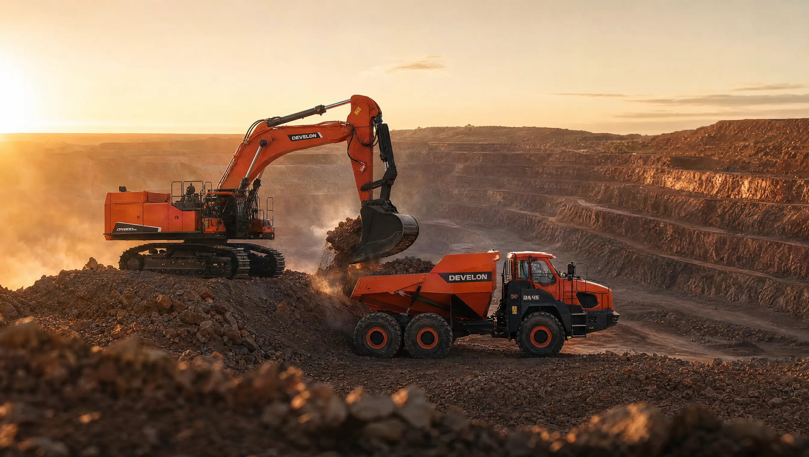 A wide open pit at first light, an excavator loading an articulated dump truck on the bench amid dust